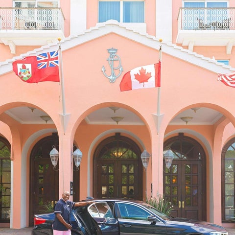 A pink-colored hotel facade features arched entrances, multiple flags, and a dark sedan parked in front.