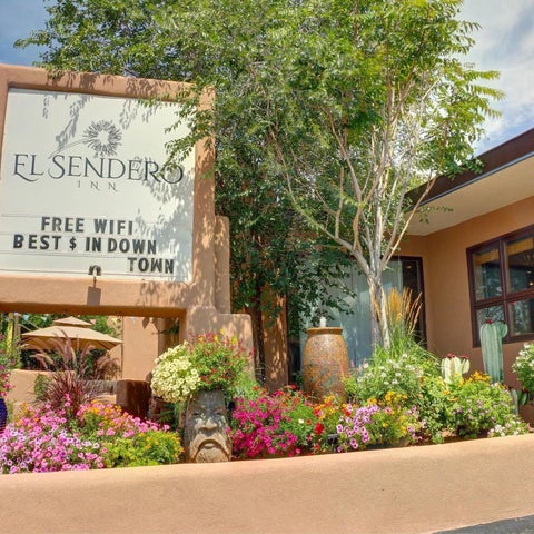 El Sendero sign features a southwestern-style facade with landscaping, umbrellas, and a window view of the property.