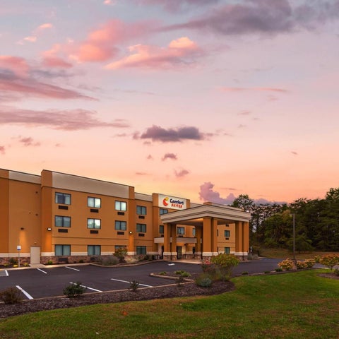 A Comfort Suites hotel is shown with a sign and landscaping under a colorful sunset sky.