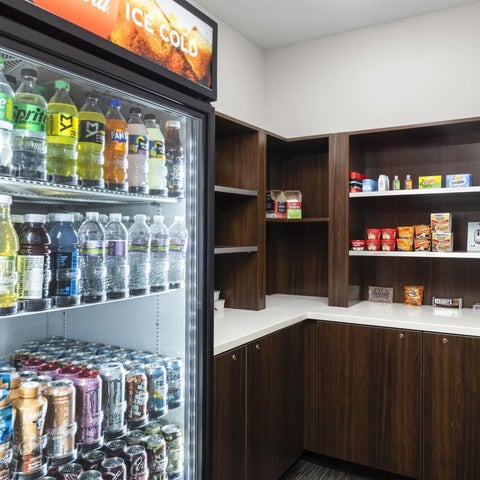 A hotel convenience area features a refrigerator stocked with beverages and shelves filled with snacks and dry goods.