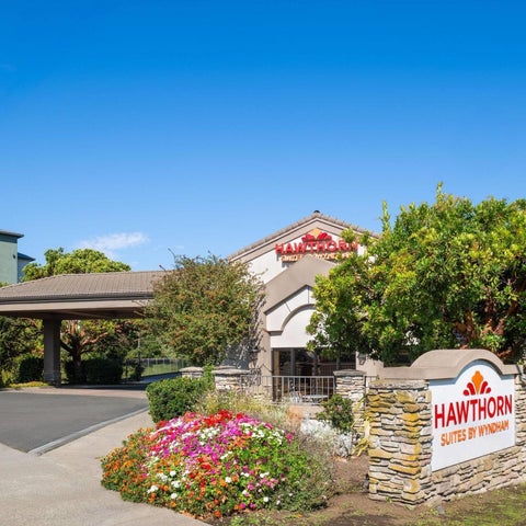 The exterior of the Hawthorn Suites by Wyndham hotel features a brick facade, landscaping, and a sign with colorful flowers.