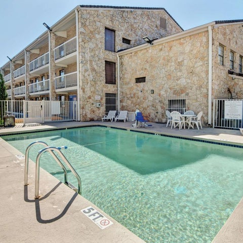 A rectangular swimming pool with lounge chairs and a light-colored building with balconies in the background.