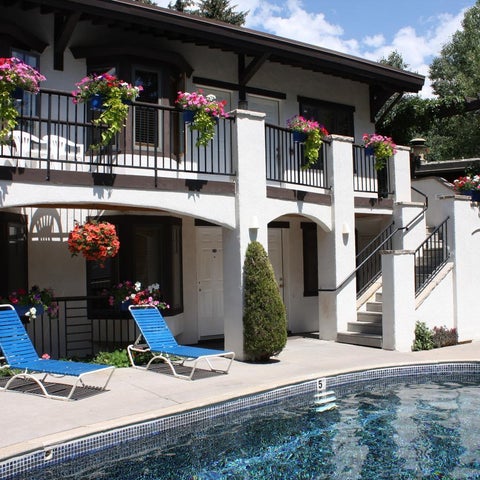 A white stucco building features a balcony adorned with flower boxes and a pool with lounge chairs in the foreground.