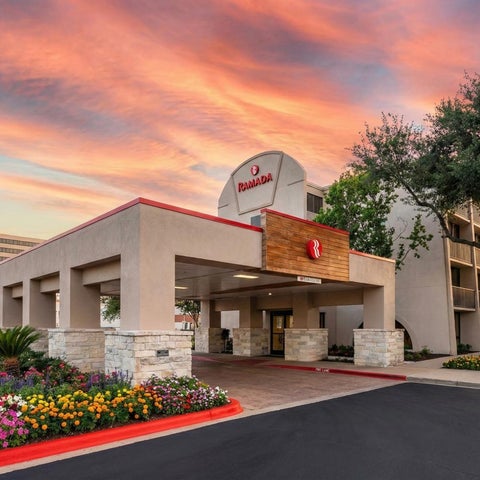 A Radisson hotel entrance features a covered walkway, landscaped gardens, and American flags against a colorful sunset sky.