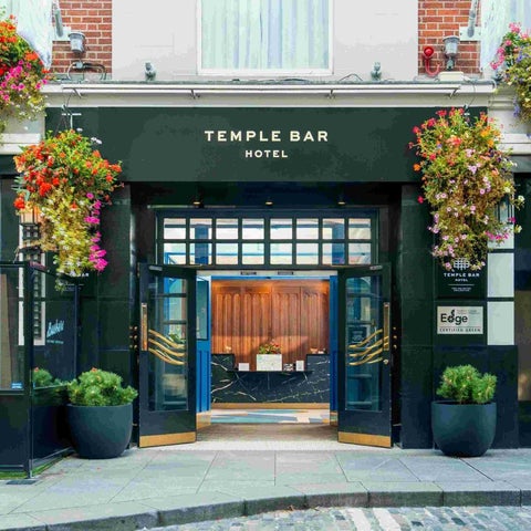 The Temple Bar Hotel's entrance features a dark facade, large glass doors, and vibrant floral arrangements on either side.