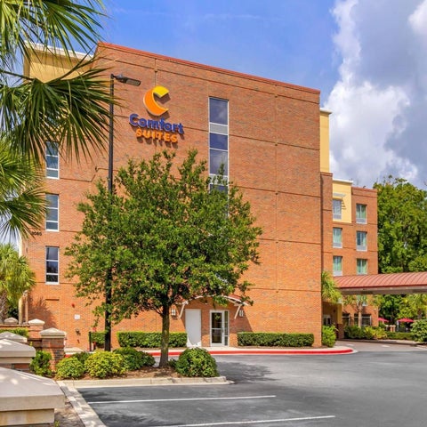 A Comfort Suites hotel building with palm trees and landscaping is shown with a parking lot in front.