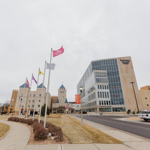 A large, modern hotel or convention center is seen with flags and a landscaped area in front of it.