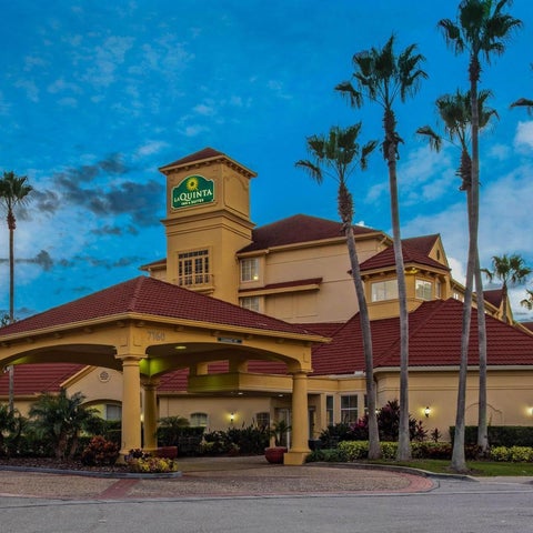 A La Quinta Inn & Suites building with a red tile roof and palm trees is seen against a blue dusk sky.