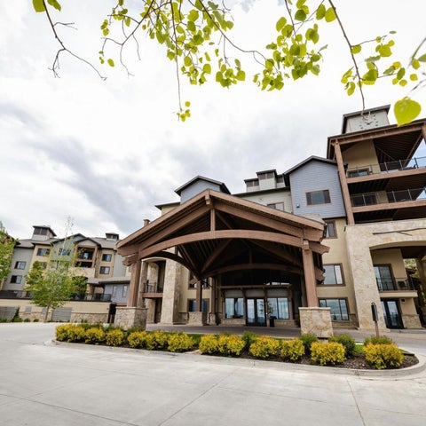A modern apartment complex with a large entryway and multiple balconies is seen under a partly cloudy sky.