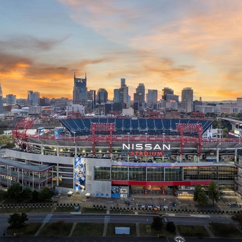 An aerial view showcases Nissan Stadium and the Nashville skyline at sunset, with city buildings and roads visible.