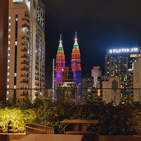 A nighttime view showcases Kuala Lumpur's skyline, featuring the Petronas Twin Towers illuminated with colorful lights.