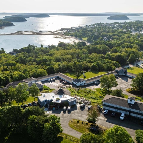 An aerial view showcases a sprawling hotel complex nestled amongst lush greenery, overlooking a bay with several islands.