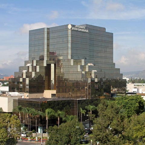 A large, modern office building with a distinctive tiered design and extensive glass facade is seen against a backdrop of mountains.