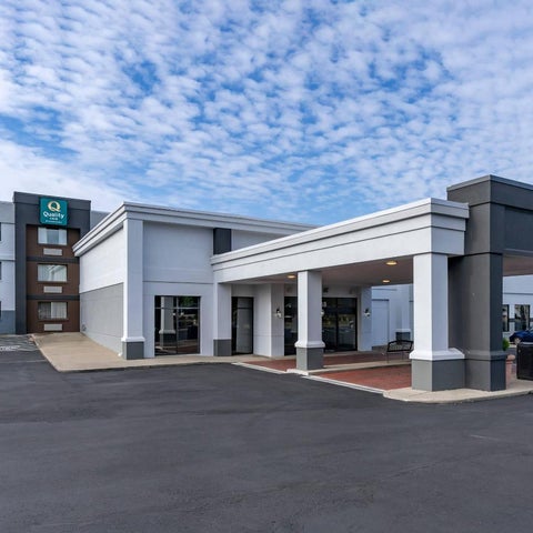 A modern hotel building features a covered entrance and parking area under a large overhang.