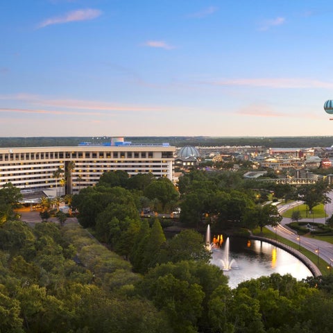 An aerial view showcases a large resort complex with multiple buildings, lush greenery, a fountain, and a hot air balloon in the distance.