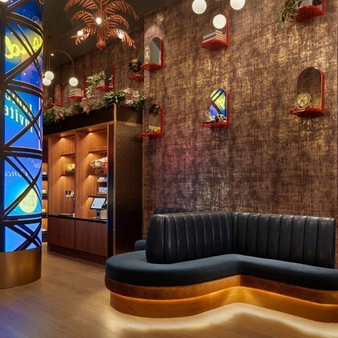 A modern lobby features a blue and gold cylindrical art installation, a dark blue sectional sofa, and wooden shelving with decorative elements.
