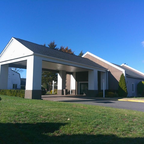 A large building with a prominent covered entrance and manicured landscaping under a clear blue sky.