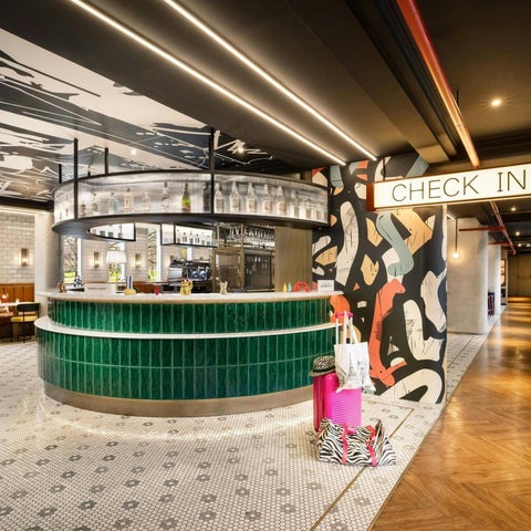 A brightly lit lobby features a curved green reception desk with a checkered floor and abstract wall art.