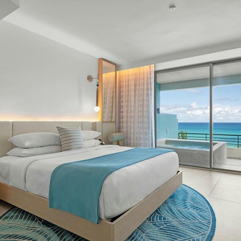 A modern hotel room features a king-size bed, a balcony with ocean view, and a stylish rug.