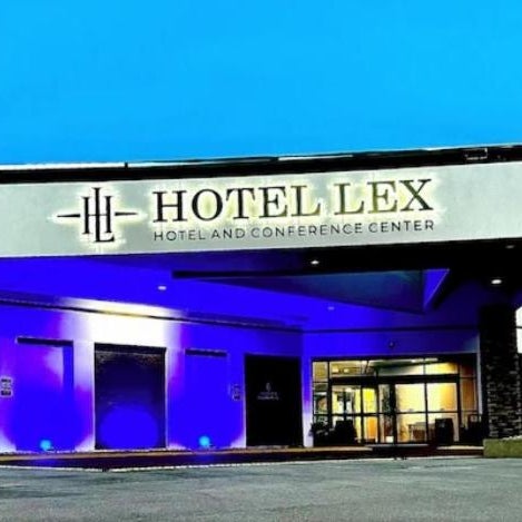 Hotel Lex and Conference Center's facade features a modern design with stone pillars and blue-lit entrances under a clear sky.