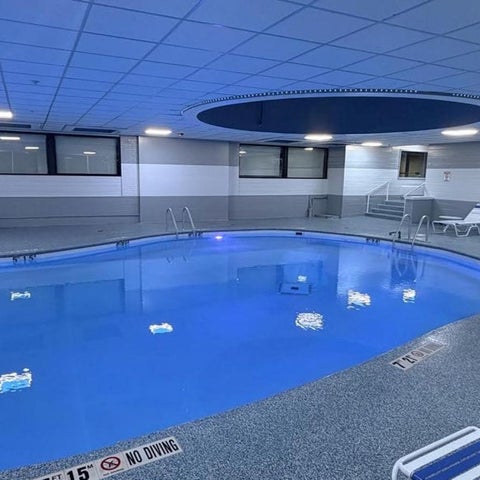 An indoor pool with blue lighting and lounge chairs surrounds the pool area, featuring a diving depth marker.