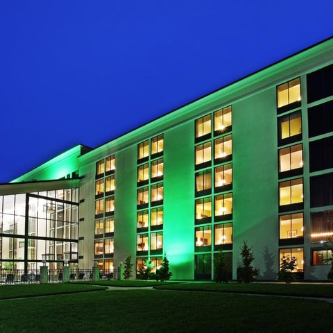 A modern building with illuminated windows and a glass-enclosed entrance is seen at dusk against a blue sky.