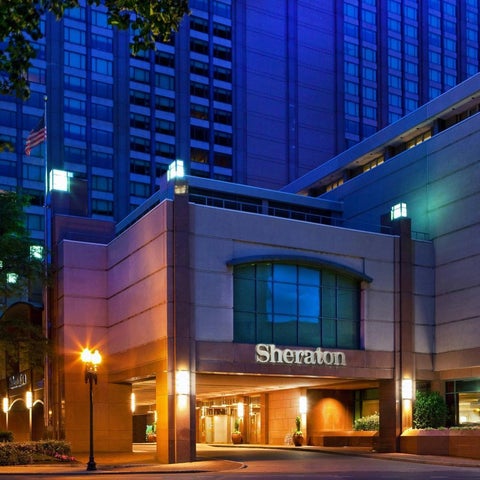 The entrance of a Sheraton hotel is illuminated at dusk, showcasing its modern architecture and signage.
