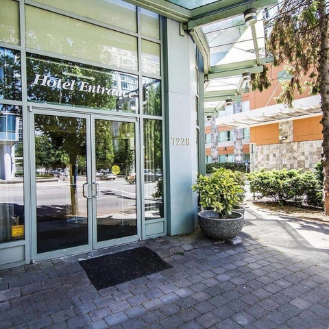 The hotel entrance features glass doors, a brick walkway, and a sign indicating 'Hotel Entrance' with a building number.