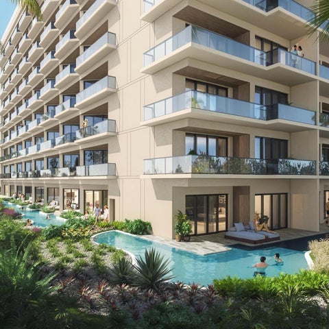 A modern hotel features a large, turquoise pool surrounded by lush greenery and lounge chairs, with balconies overlooking the water.
