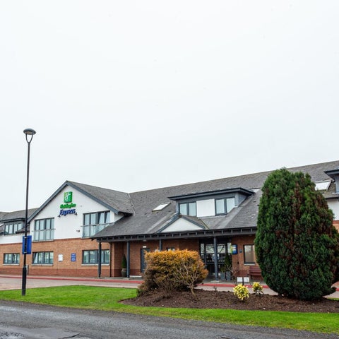 A view of the Holiday Inn hotel exterior, showcasing its facade, parking area, and surrounding landscaping on a cloudy day.