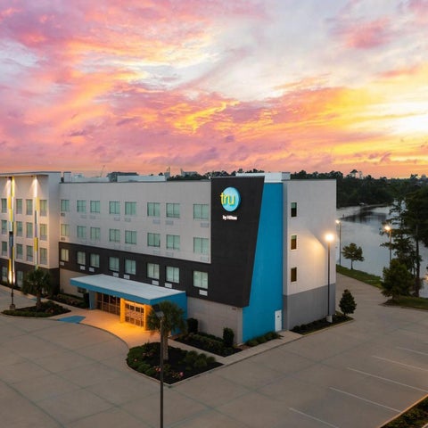 A multi-story hotel building with a modern design is illuminated by a vibrant sunset sky.