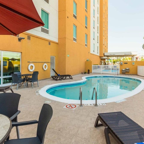 An outdoor pool area with lounge chairs, tables, and umbrellas is situated next to a yellow hotel building.