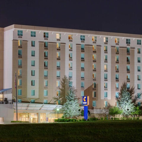 A brightly lit Comfort Inn hotel building stands against a dark night sky with trees and a covered entrance visible.