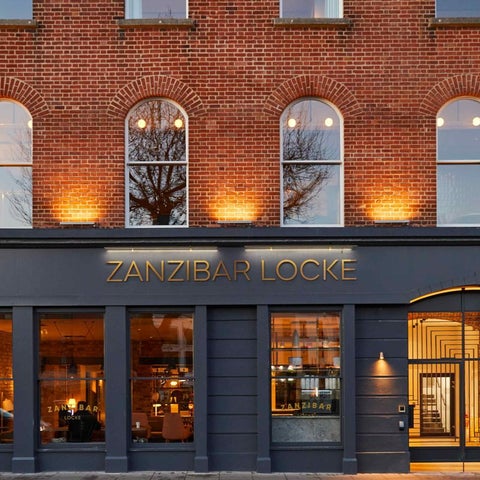 The facade of Zanzibar Locke features a brick building with arched windows and a dark blue entrance with signage.