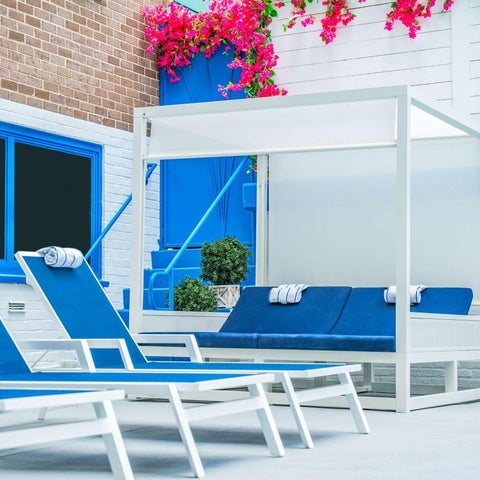 A poolside area features blue lounge chairs, a white cabana, and vibrant bougainvillea flowers against a white brick wall.