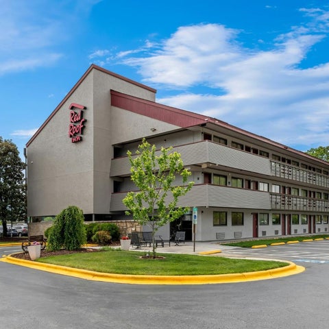 A red-brick motel with a three-story building facade, a manicured lawn, and a parking lot under a partly cloudy sky.
