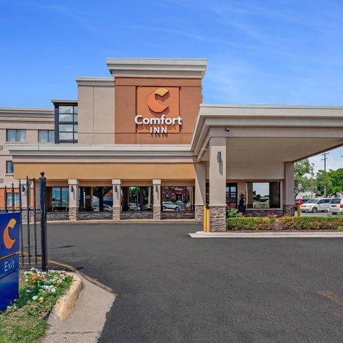 A Comfort Inn hotel facade is shown with a covered entrance, signage, and a parking lot in front of the building.