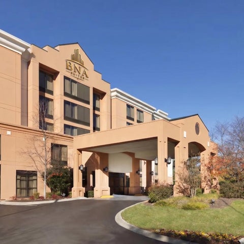 A large, tan-colored hotel building with a covered entrance and an American flag flying nearby on a clear day.