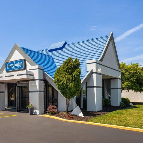 A Travelodge by Wyndham building features a blue roof, white facade, and landscaping with trees and shrubs.