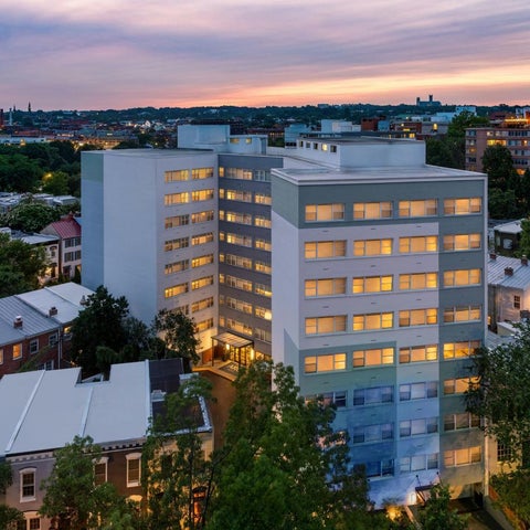 An elevated view showcases a modern building with numerous windows and surrounding residential structures at dusk.