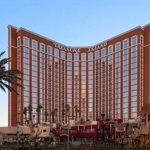 The Treasure Island Hotel and Casino building features a curved facade with numerous windows and palm trees in the foreground.