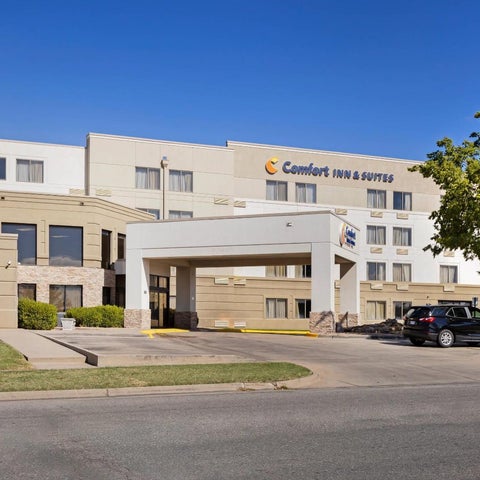 A beige Comfort Inn & Suites building with a covered entrance and parking lot under a clear blue sky.