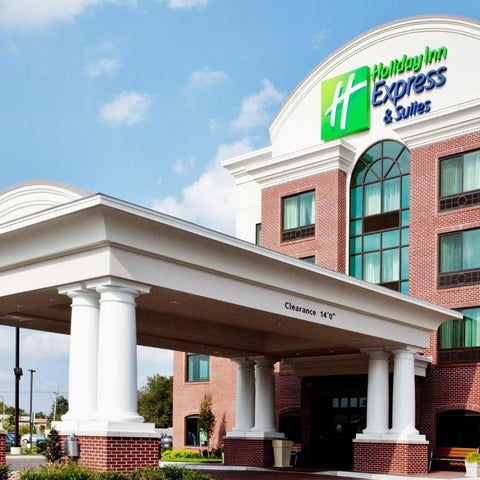 A Holiday Inn Express & Suites building features a brick facade, arched entryway, and a covered drop-off area with prominent signage.