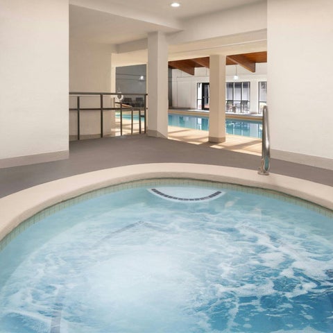 A circular jacuzzi with bubbling water is situated on a tiled floor, with a pool visible through a large window.