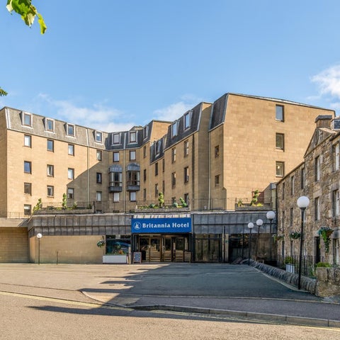The Britannia Hotel is shown with its entrance and facade, featuring a modern design and surrounding greenery.
