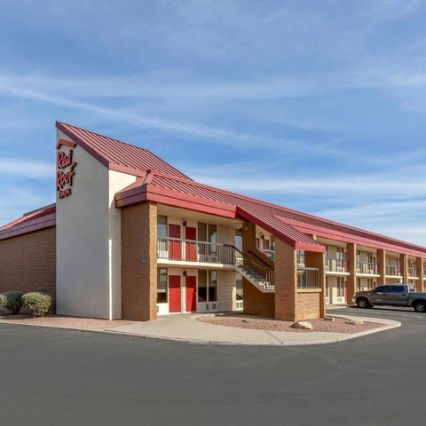 A Red Roof Inn motel building is shown with a red roof and beige facade, parked cars, and a cloudy sky.