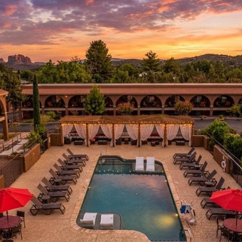An aerial view showcases a rectangular pool surrounded by lounge chairs, cabanas, and umbrellas at a resort during sunset.