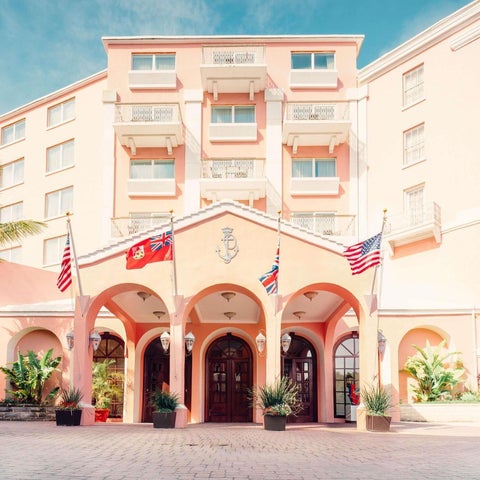 A pink-colored hotel building with arched entrances and flags displayed in front of a bright blue sky.