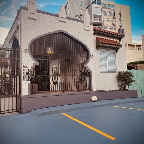 A building facade with a distinctive arched entrance and decorative metal gate, featuring a numbered plaque and surrounding greenery.
