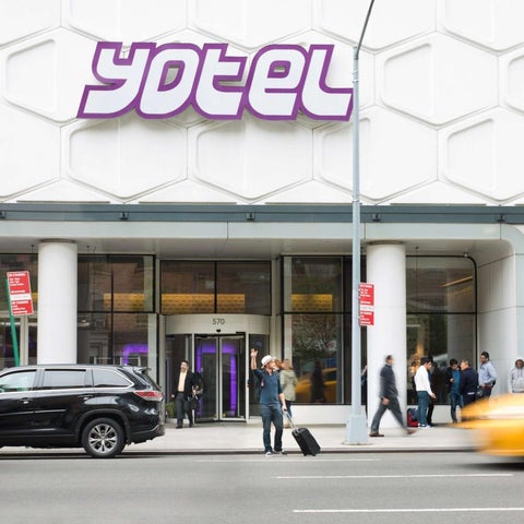 The yotel hotel's facade features a honeycomb pattern and a busy street with pedestrians and vehicles passing by.